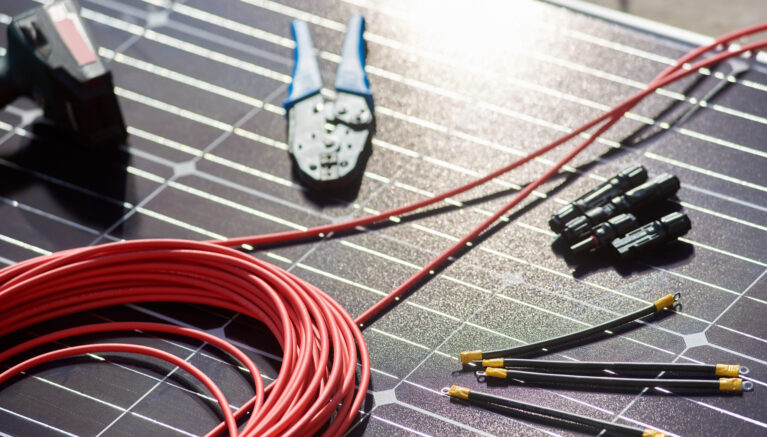 Close-up view of different details and instruments for mounting and connecting solar photovoltaic system. Objects laying on blue solar panel. Alternative energy resources renewable ecologycal concept.