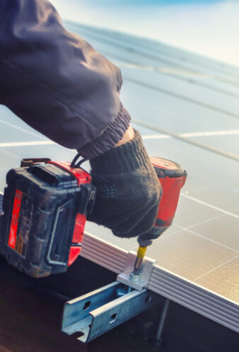 Solar panel technician with drill installing solar panels on roof.  technician in blue suit installing photovoltaic blue solar modules with screw. Electrician panel sun sustainable resources