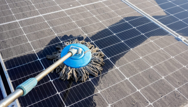Man clean up the solar panels that are dirty with dust and birds' droppings to improve the efficiency of solar energy storage.