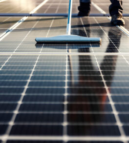 Cropped picture of broom and legs with solar panels. A worker is cleaning solar panels.