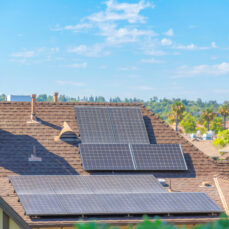 Solar panels on top of the asphalt composite shingles roof of a house at Ladera Ranch, California. Roof of a house in a residential community with palm trees outdoors against the sky.